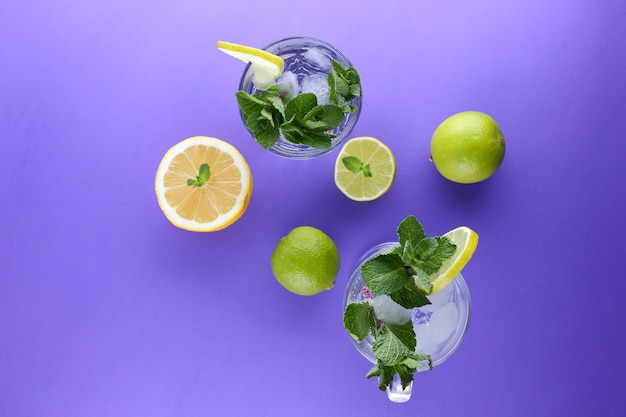 Glass of mojito with ice and mint Closeup of cocktails with different types of citrus fruits on a purple background