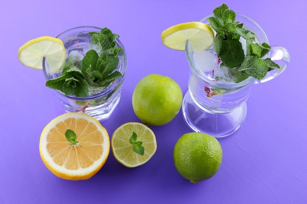 Glass of mojito with ice and mint Closeup of cocktails with different types of citrus fruits on a purple background