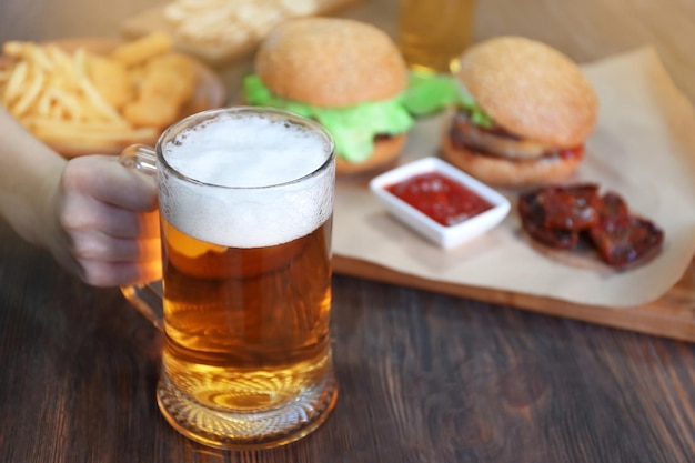 Glass mug of light beer with snacks on dark wooden table close up