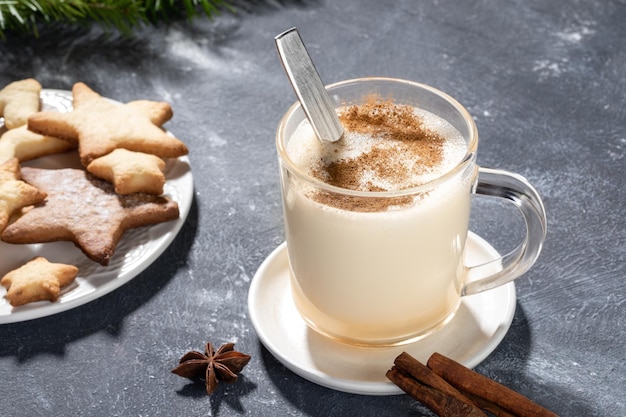 Photo glass mug with christmas drink eggnog and heart shape cookies on wooden kitchen board on grey