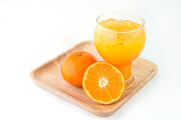 A glass of orange juice and orange on wooden plate.