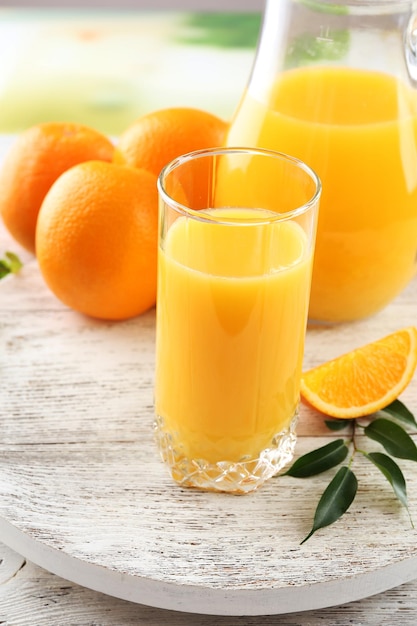 Glass of orange juice and oranges on color wooden table background