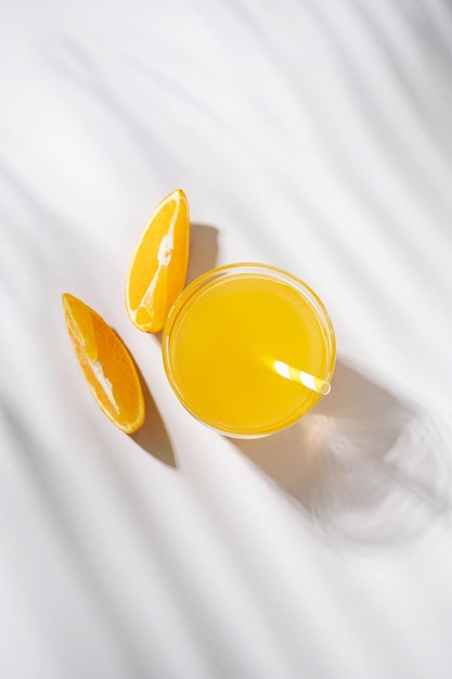 A glass of orange juice and a slice of orange on a light table with palm leaf shadow Summer time Top view and copy space Vertical orientation