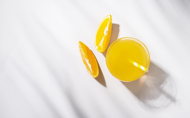 A glass of orange juice and a slice of orange on a light table with palm leaf shadow Summer time Top view and copy space