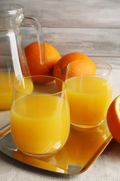 Glass of orange juice with slices on metal tray on table with tablecloth and color wooden wall background