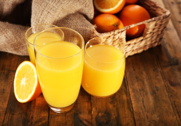 Glass of orange juice with slices and wicker basket with burlap cloth on wooden table background