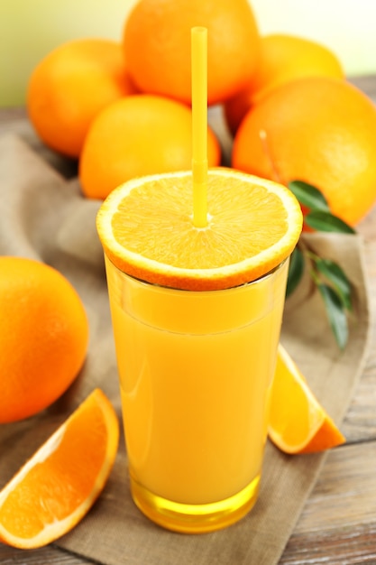 Glass of orange juice with straw and slices on wooden table