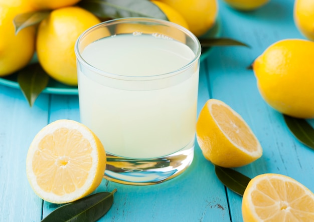 Glass of organic fresh lemon juice with raw lemons on blue wooden