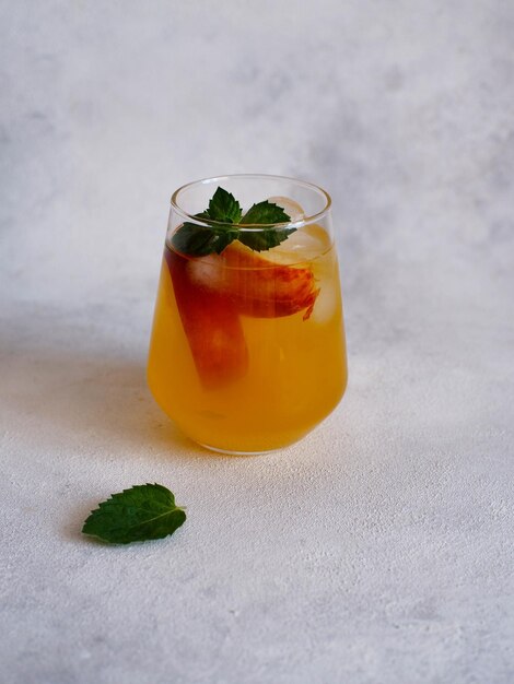 A glass of peach cocktail with ice mint leaves on a gray background Bar concept and summer drinks concept