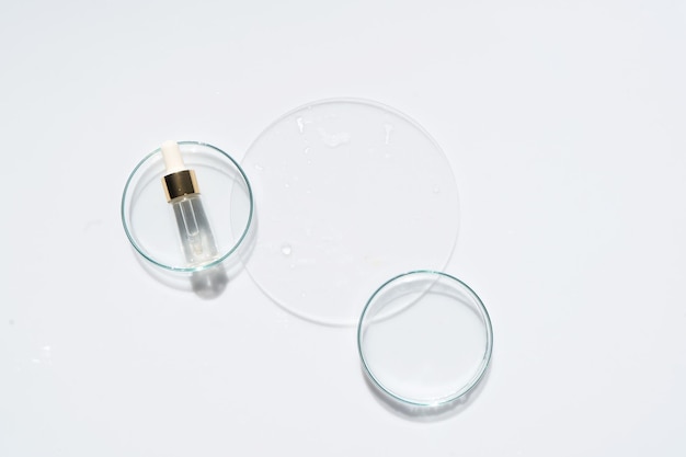 Glass petri dish with transparent pure serum for skin care on white background top view Laboratory tests and research making and testing cosmetic