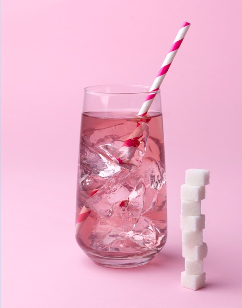 Photo glass of pink soda water with ice and striped straw with sugar cubes at pink table.