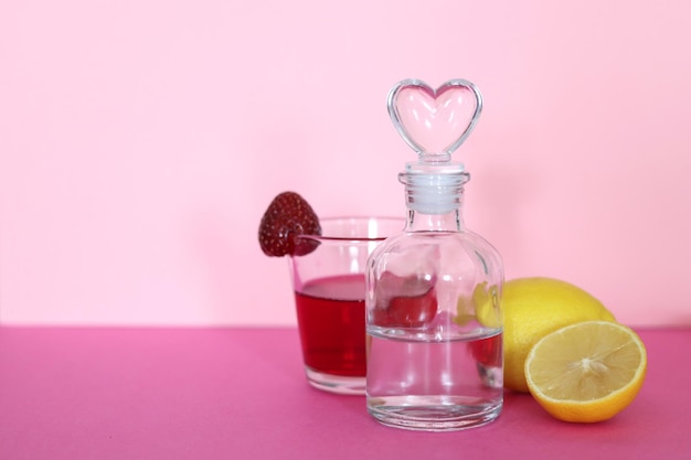 a glass of a red drink with a strawberry and a bottle with a clear liquid with a heart shaped plug