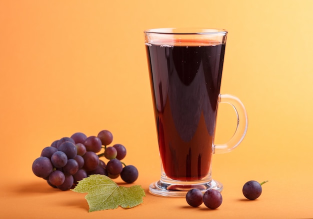 Glass of red grape juice on orange background. Side view