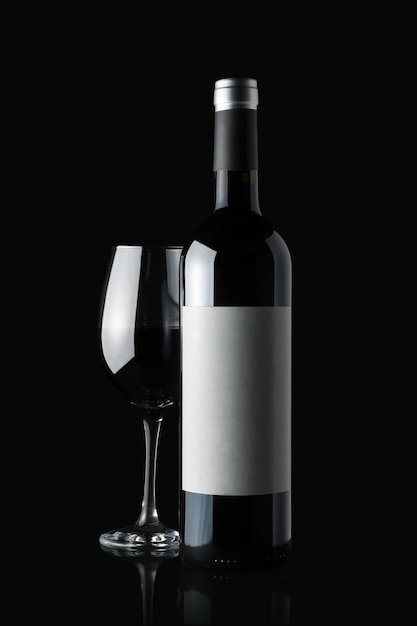 Glass of red wine next to a bottle isolated on black wall