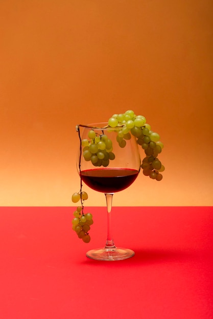 A glass of red wine and a bunch of grapes on a colored background