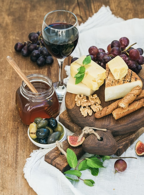 Glass of red wine, cheese board, grapes,fig, strawberries, honey and bread sticks  on rustic wooden table