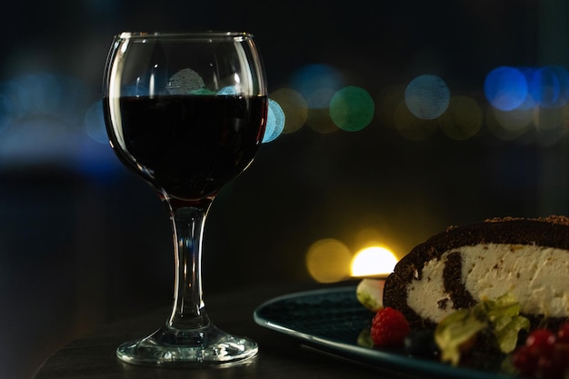 Glass of Red Wine and Chocolate Cream Cake with Berries Night City Bokeh Lights in Background