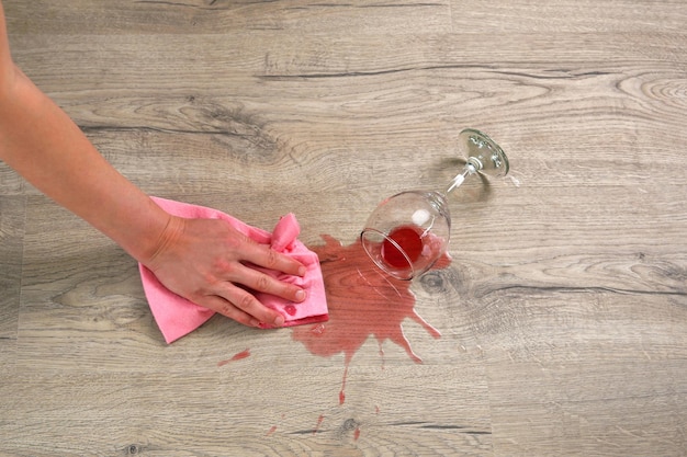 Glass of red wine fell on laminate wine spilled on floor A woman wipes the laminate from moisture