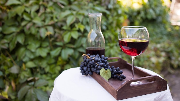 A glass of red wine prepared for tasting stands on a table with a white tablecloth outdoors in sunlight