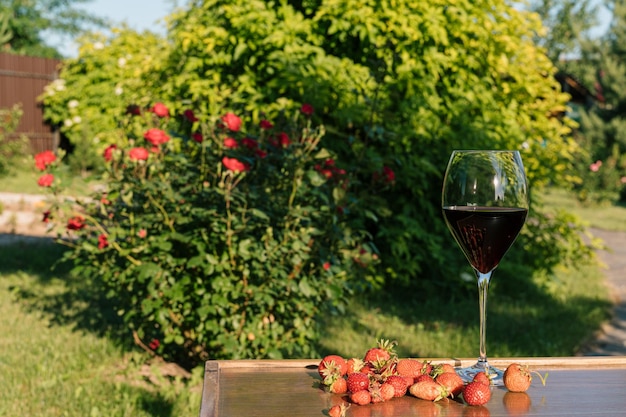 A glass of red wine and strawberries against outdoor garden background