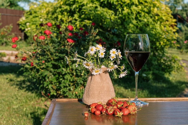 A glass of red wine and strawberries against outdoor garden background