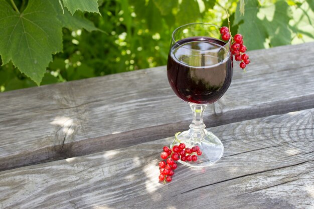 Glass of red wine with red currants on nature, wine making concept