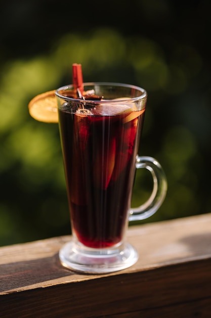 A glass of red wine with a slice of orange on the rim sits on a wooden railing.