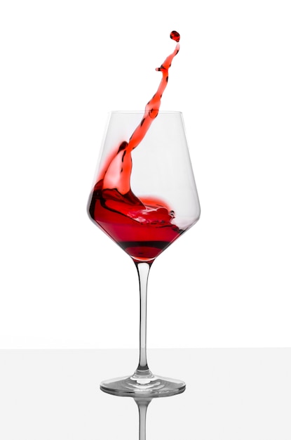 Glass of red wine with splashes on white table.