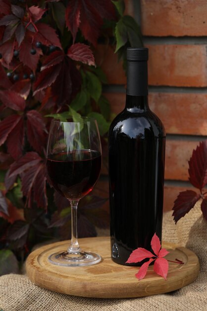 glass of red wine on wooden background with autumn leaves and bottle