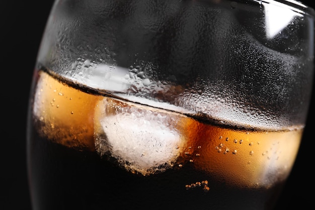 Glass of refreshing cola with ice on black background closeup