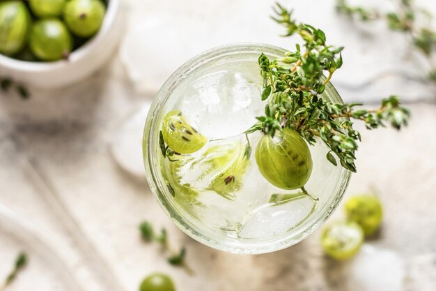 Glass of refreshing iced detox drink with gooseberries and thyme Infused water or cocktail close up