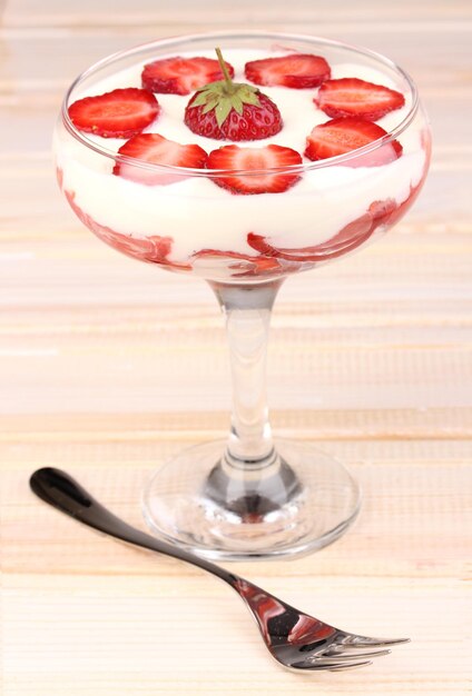 Glass of ripe strawberries with cream on wooden background