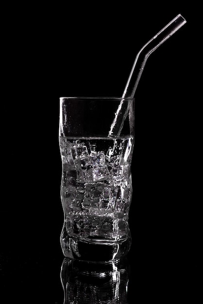 Glass of sparkling water soda drink with ice on black background. Pouring clear water in glass on black background