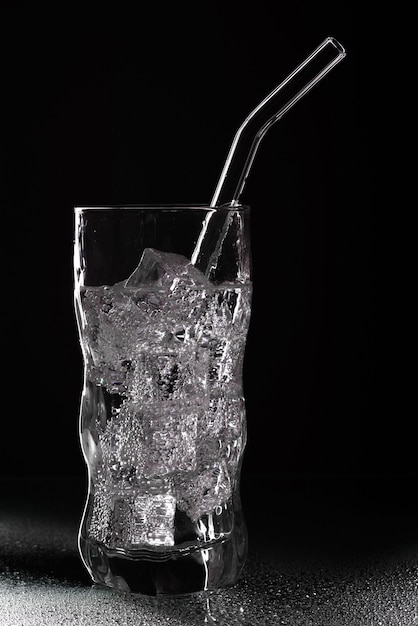 Glass of sparkling water soda drink with ice on black background. Pouring clear water in glass on black background