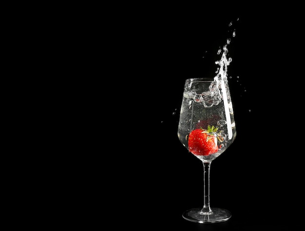 Glass of splashing drink with red strawberry on black