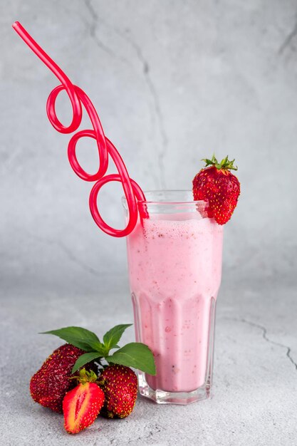 Glass of strawberry cocktail with straw on gray background