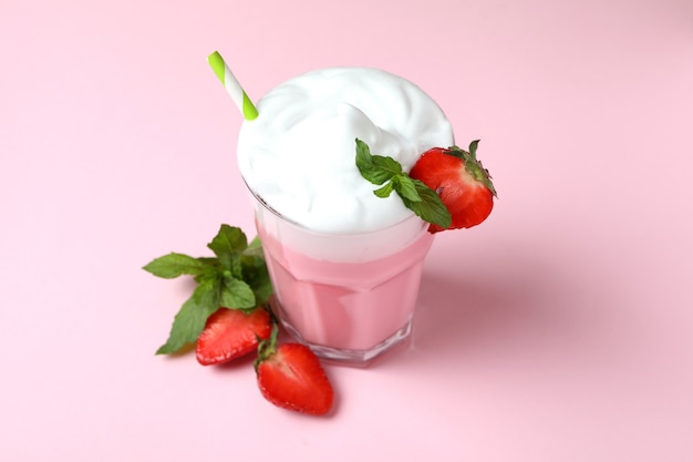 Glass of strawberry milkshake and ingredients on pink background