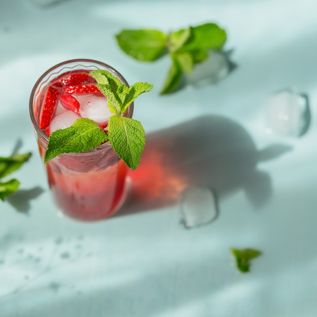 Glass of strawberry soda drink on light blue background