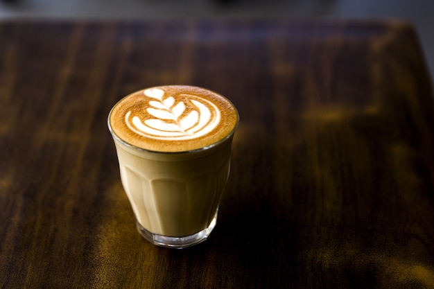 Glass of tasty cappucino with latte art on wooden table background. Morning drink