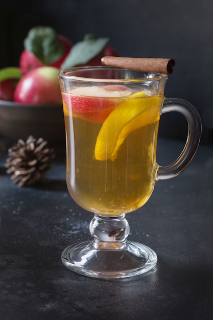 Glass of tea with lemon, spiced, sliced apple and cinnamon on black board. Autumn still life.