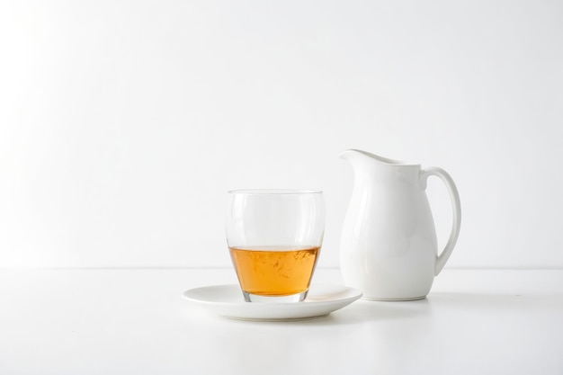 Photo glass of tea with white saucer and pitcher on white table