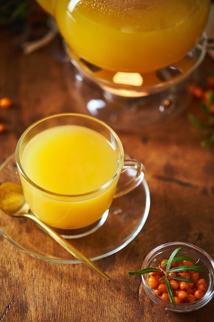 Glass teapot and sea buckthorn tea cup on wooden background