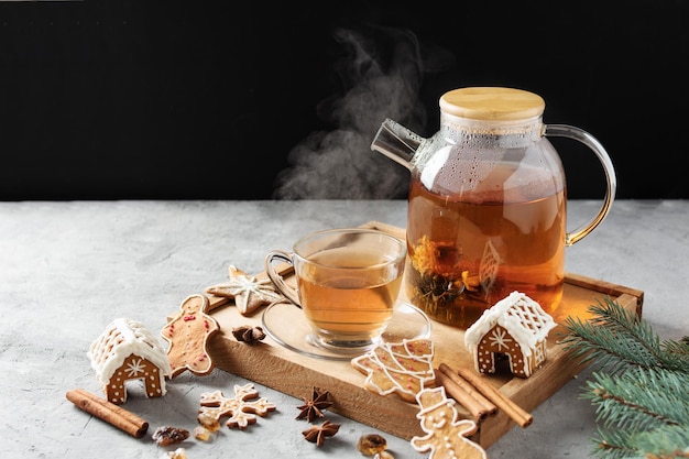 Glass teapot with blossoming tea and tea cup on grey table with Christmas gingerbread cookies