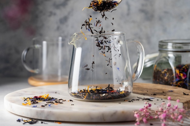 A glass teapot with a cup of tea being poured into it.