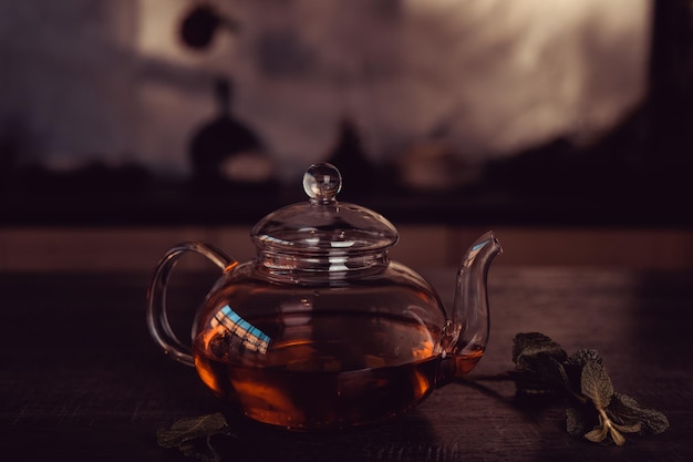 A glass teapot with red tea and fresh mint on the table