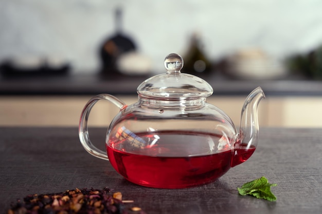 A glass teapot with red tea and fresh mint on the table