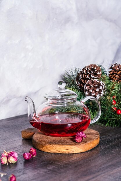 A glass teapot with red tea standing on a table decorated with a fir branch