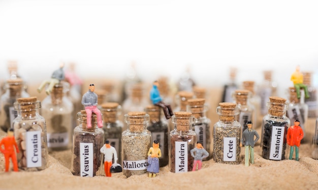 Glass test-tube with sand of different summer vacation destinations. Located in sand with small people figures.