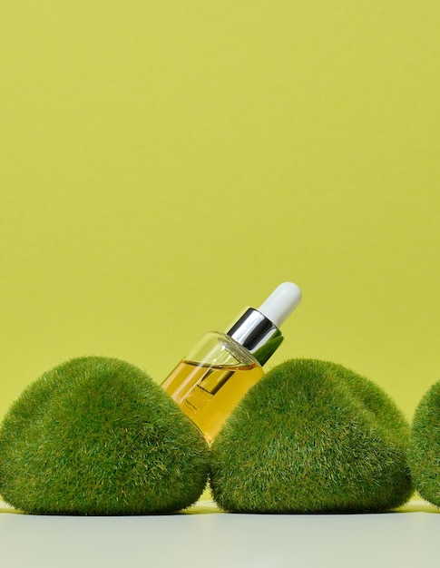 Glass transparent bottle with pipette and yellow oil on green moss