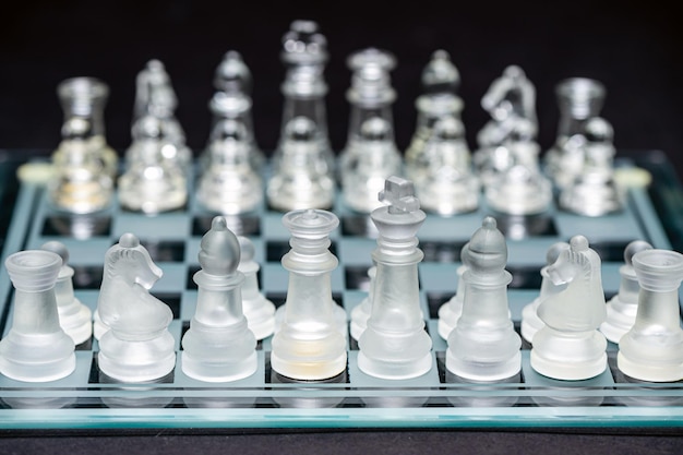 Glass transparent chess pieces on a checkerboard selective focus closeup isolated on black